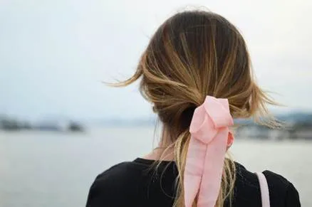 A person with a light pink ribbon tying their brown hair