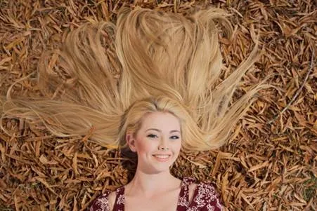 A person with blonde hair lying on autumn leaves and smiling